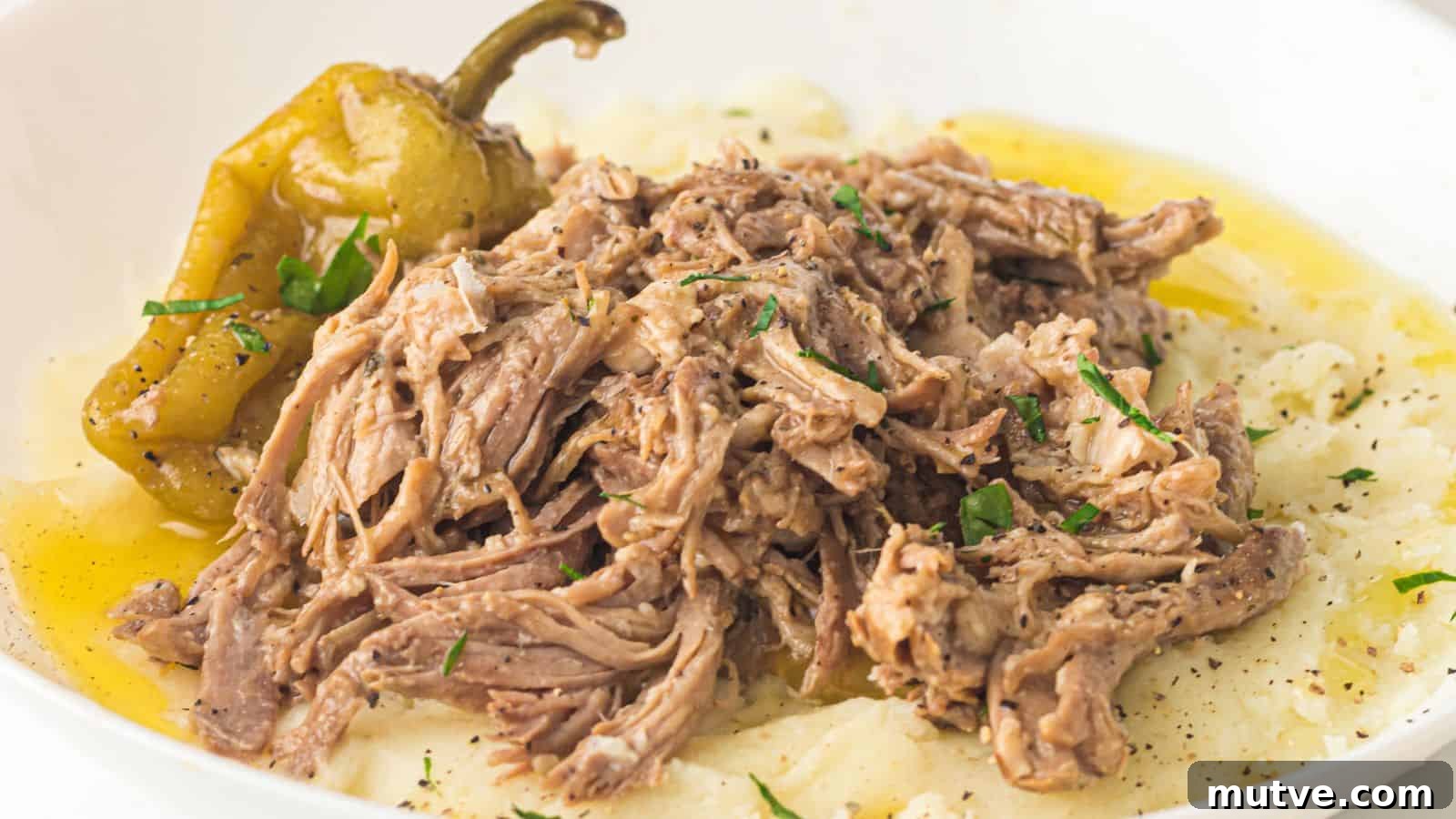 Shredded roast beef served over mashed potatoes with a pepper and a light drizzle of gravy, garnished with chopped herbs.