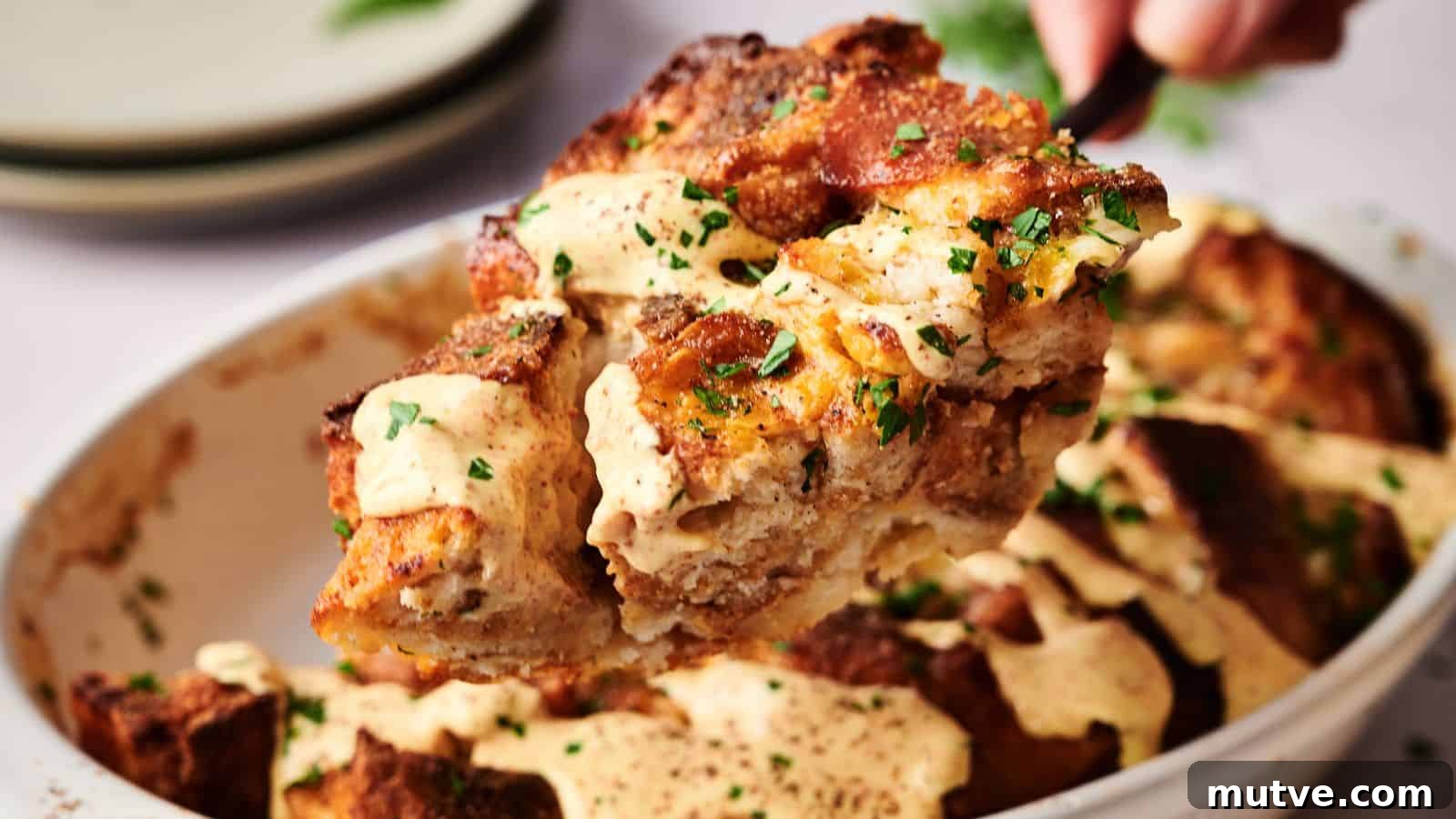 A serving of bread pudding with a creamy sauce and chopped herbs is lifted from a baking dish.