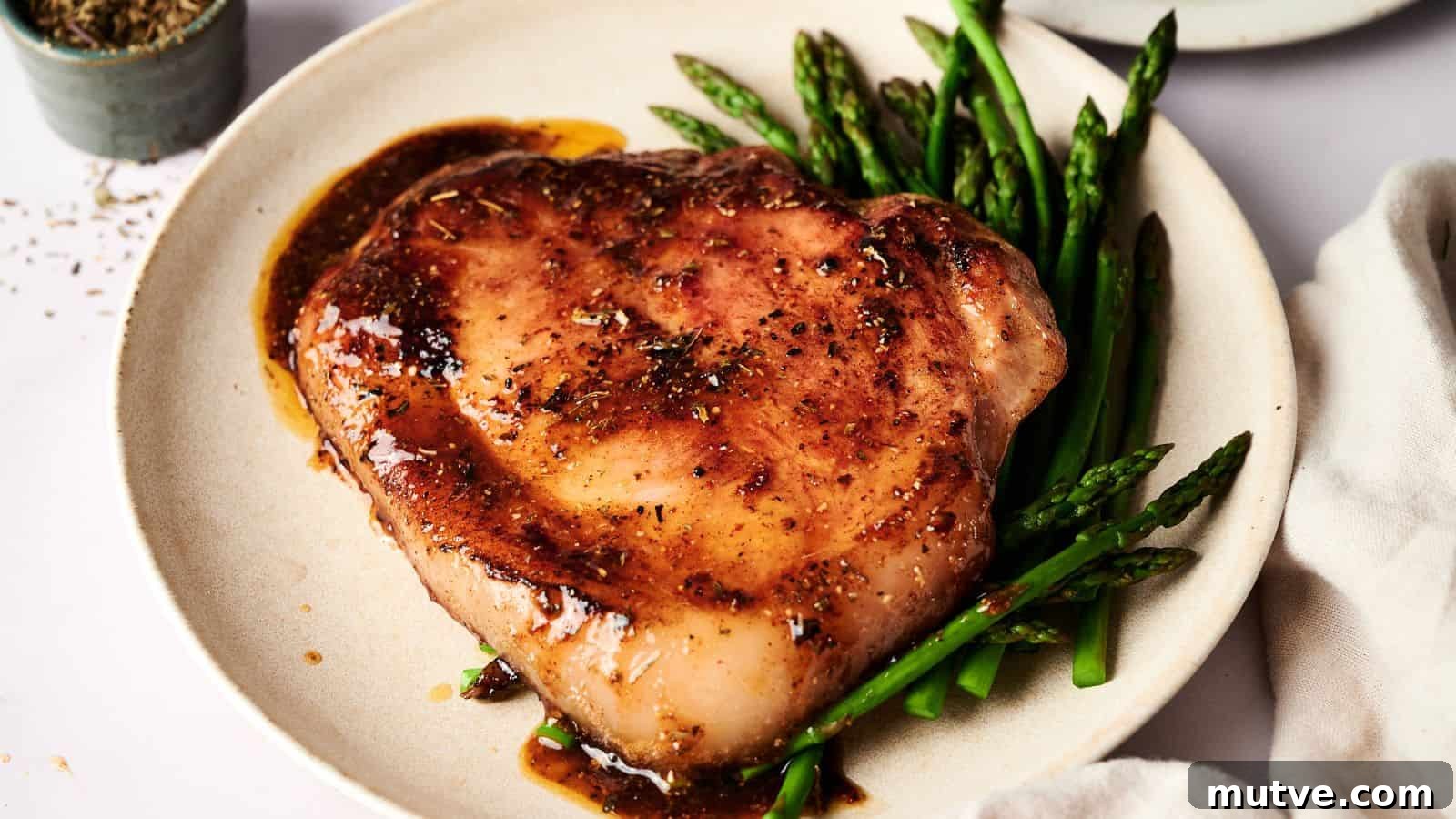 A cooked pork chop with brown sauce is served on a white plate alongside steamed asparagus spears.