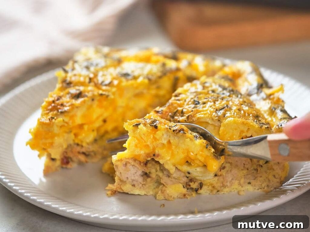 A close-up of a slice of cheesy breakfast casserole with eggs and sausage on a white plate.