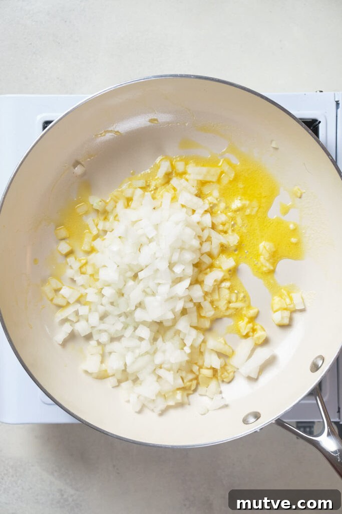 Chopped onions cooking in butter in a pan placed on a stovetop.