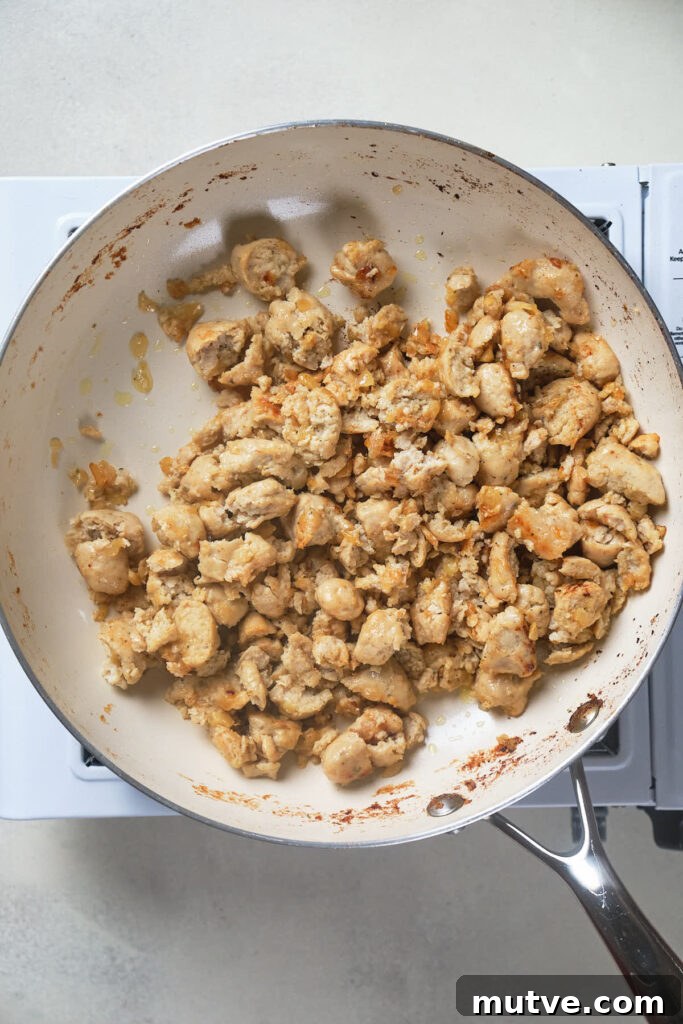 A frying pan filled with browned pieces of cooked chicken sits on a white stove.