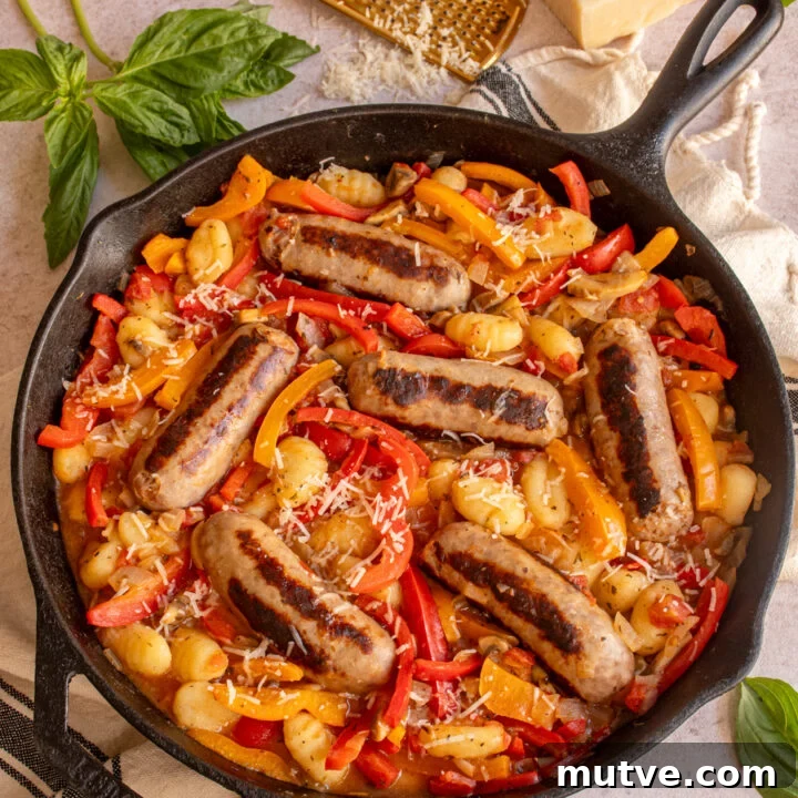 A large skillet with red and yellow bell peppers, gnocchi, and sausages.