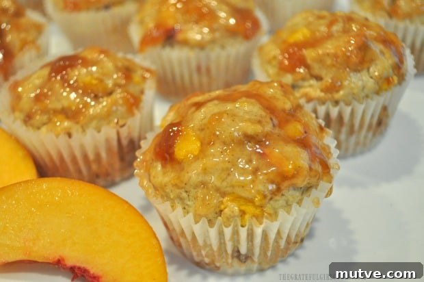 Peach Jam Muffins -The Grateful Girl Cooks! Close up photo of one peach jam muffin, with fresh peach slice in front.