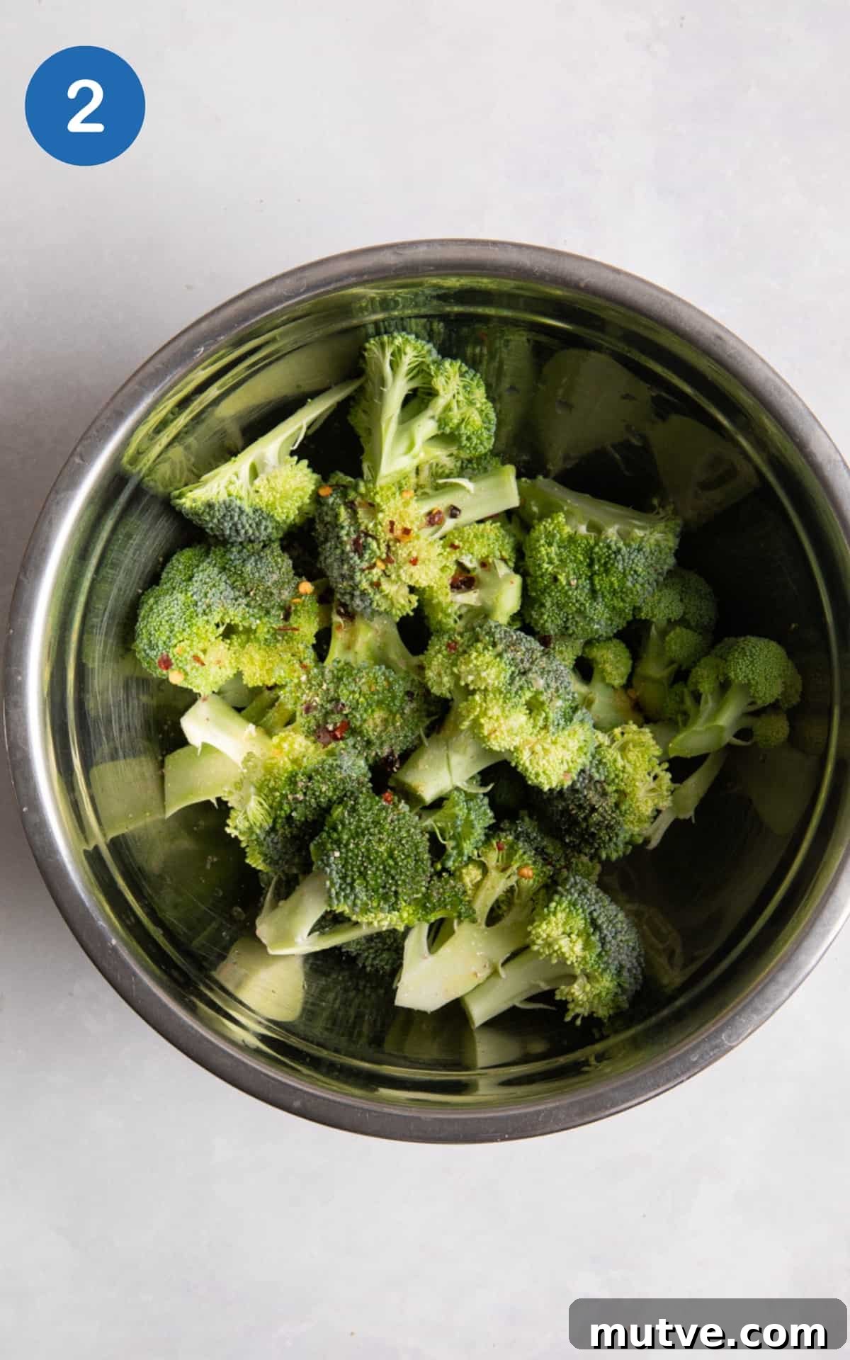 Crispy Air Fryer Broccoli in 10 Minutes 5 broccoli in large silver mixing bowl. Bowl is on white surface.