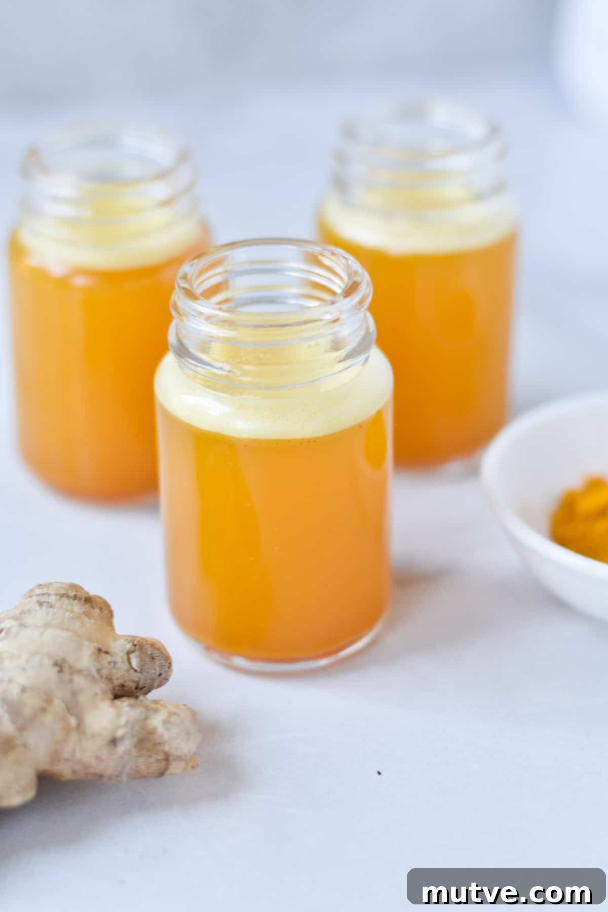 Ginger Turmeric Shots Recipe in a Blender 2 Three glass jars with an orange turmeric juice next to fresh ginger and ground turmeric.