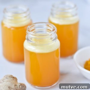 Three ginger turmeric shots in glass bottles next to fresh ginger root and turmeric.