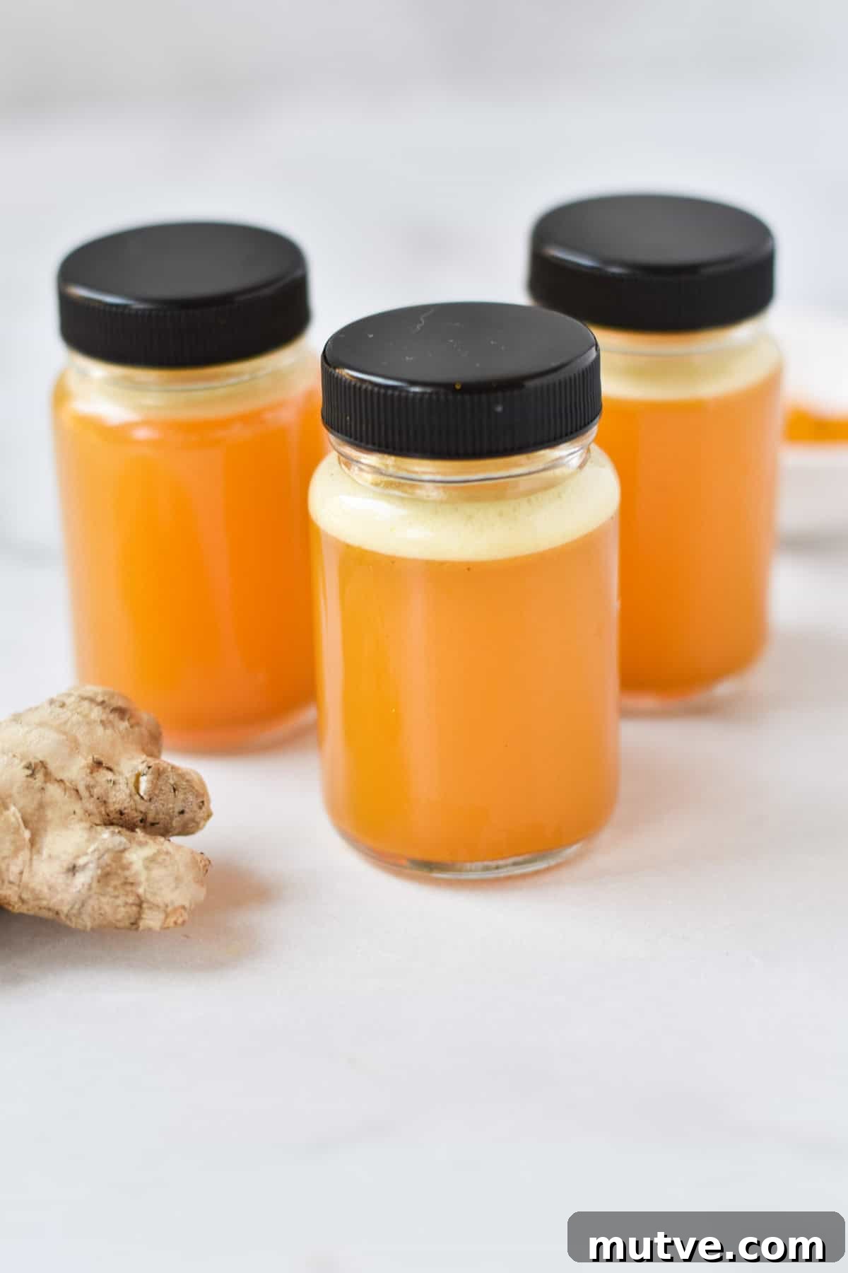 Ginger Turmeric Shots Recipe in a Blender 5 Three turmeric ginger juice bottles next to a knob of fresh ginger.
