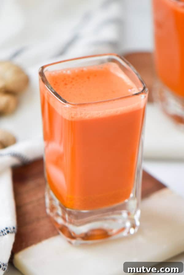 Two carrot wellness shots next to fresh ginger root.