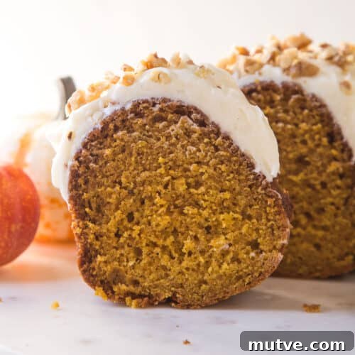 slice of pumpkin bundt cake with cream cheese frosting and chopped walnuts on top on a white marble platter.