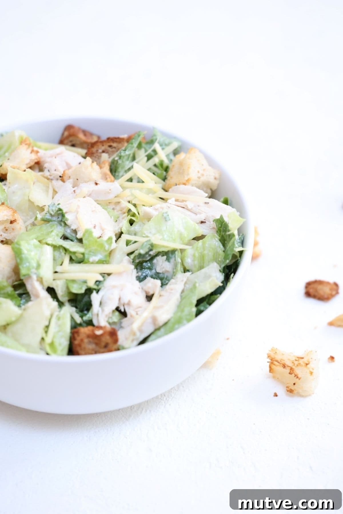 Chicken Caesar salad in a white bowl with croutons to the side.