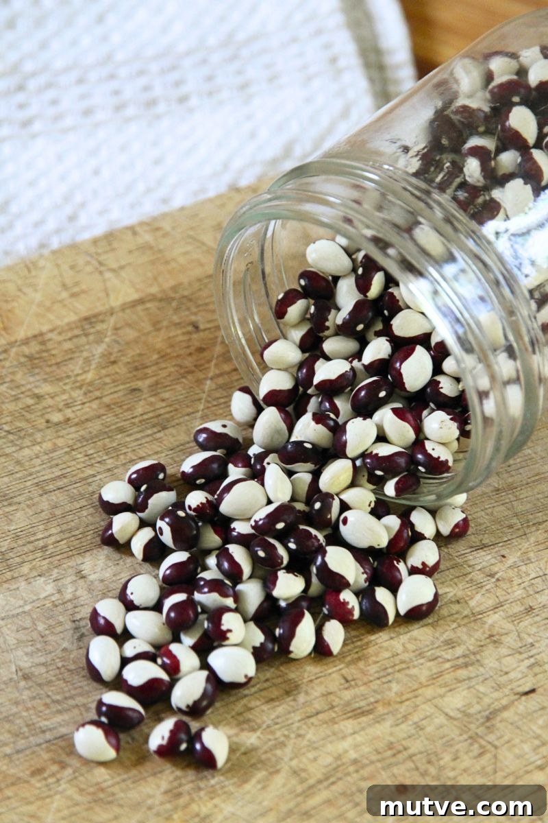 A jar of dry cranberry beans spilling out on a wooden cutting board. 