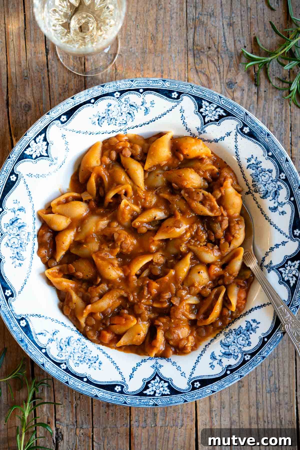 Pasta e Lenticchie Recipe: Authentic Italian Lentil Pasta 2 An overhead shot of pasta and lentils in a blue vintage style bowl on a rustic background with a glass of white wine at the side.