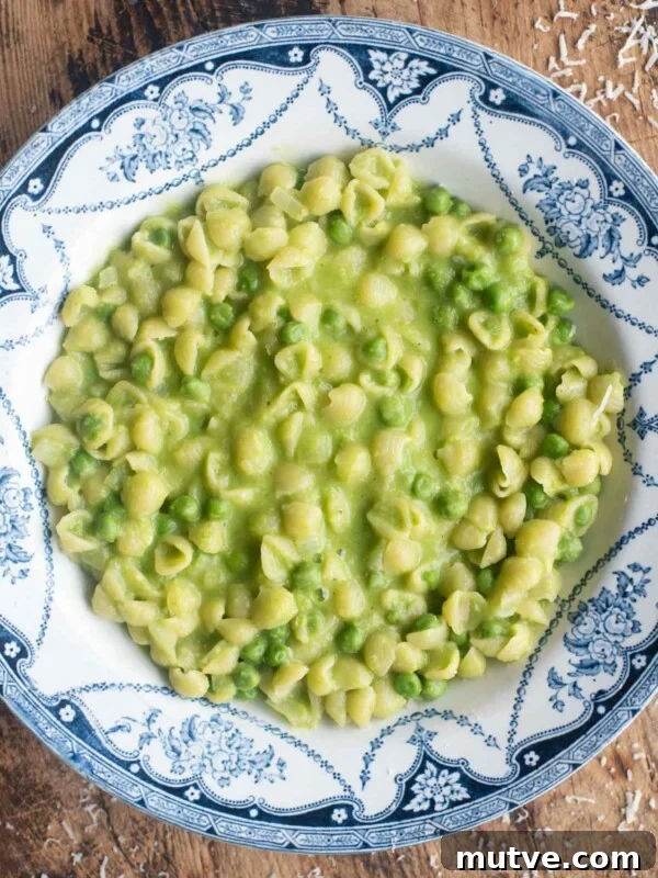 An overhead shot of Pasta and Piselli (peas) in a blue bowl sitting on a wooden surface.