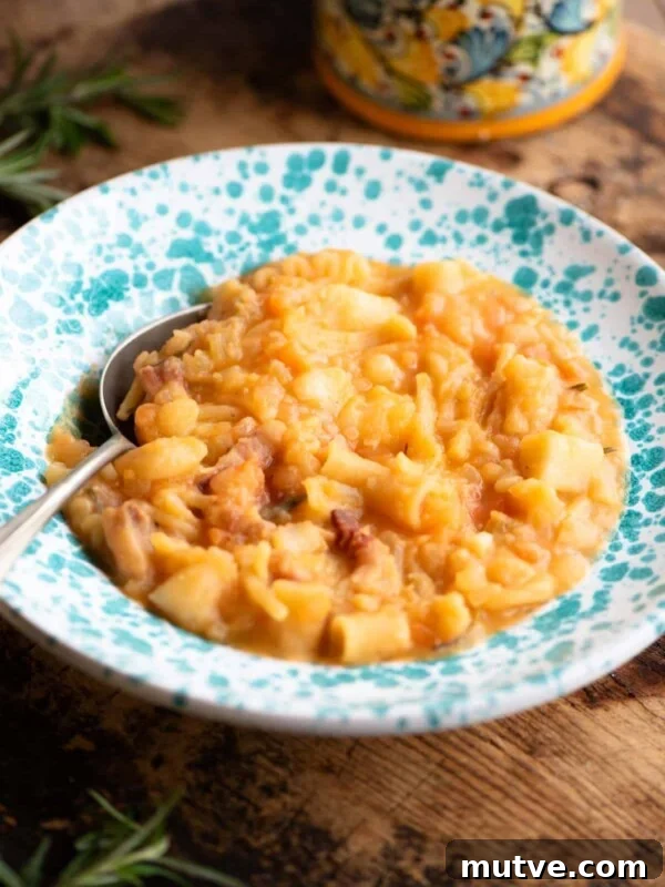Pasta e Patate (potatoes) in a blue speckled bowl with a spoon sitting on a wooden surface.