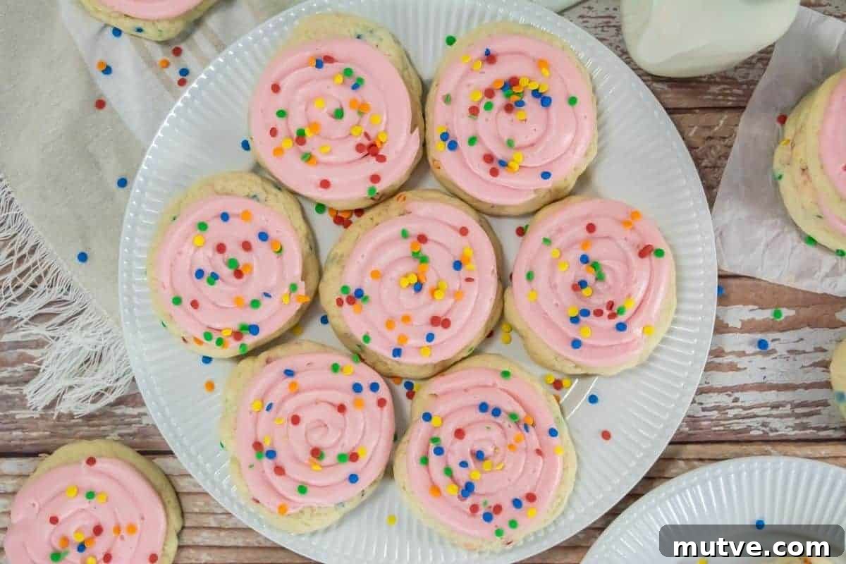 29 Halloween Treats That Beat Your Trick-or-Treat Candy 13 A plate of Copycat Crumbl Confetti Cake Cookies topped with pink frosting and multicolored sprinkles sits on a wooden table.