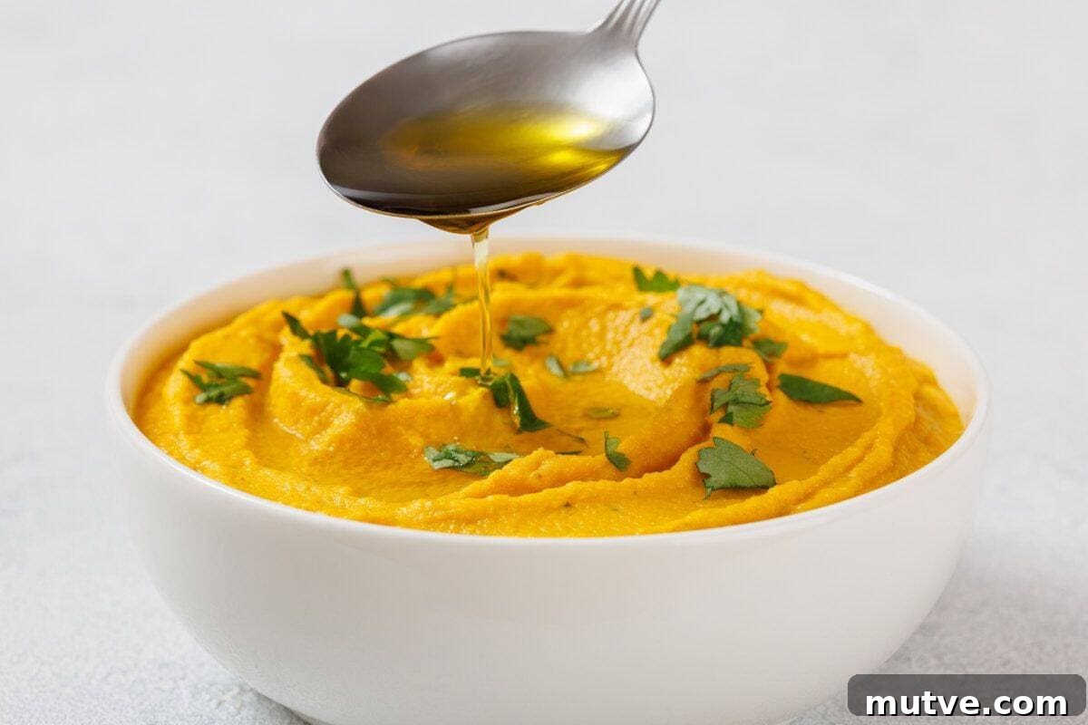 29 Halloween Treats That Beat Your Trick-or-Treat Candy 16 Bowl of Roasted Carrot Hummus garnished with green herbs, with a spoon drizzling oil above it.