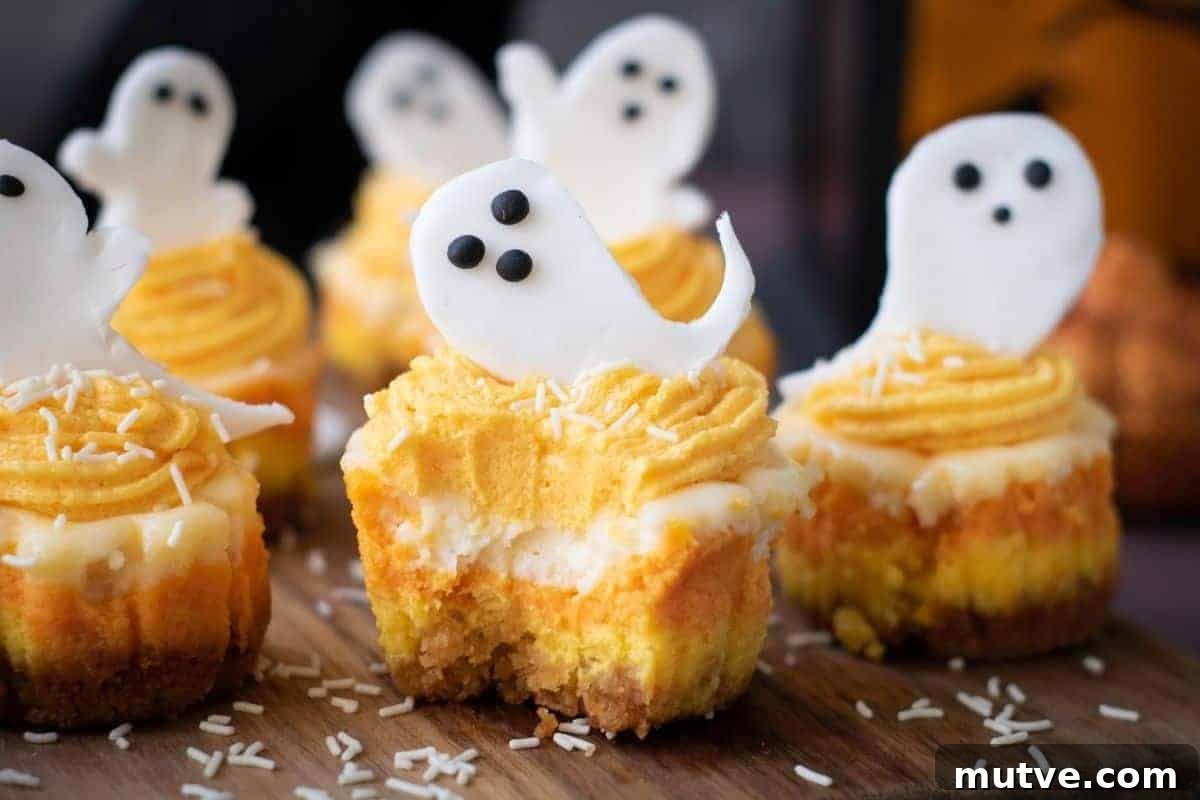 29 Halloween Treats That Beat Your Trick-or-Treat Candy 3 Mini cupcakes with orange and white frosting are topped with white ghost-shaped decorations and sprinkles, arranged on a wooden surface.