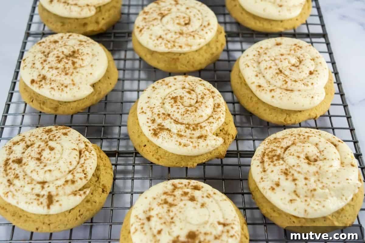 29 Halloween Treats That Beat Your Trick-or-Treat Candy 21 Copycat Crumbl Caramel Pumpkin Cookies with swirled white frosting and a sprinkle of cinnamon are cooling on a wire rack.