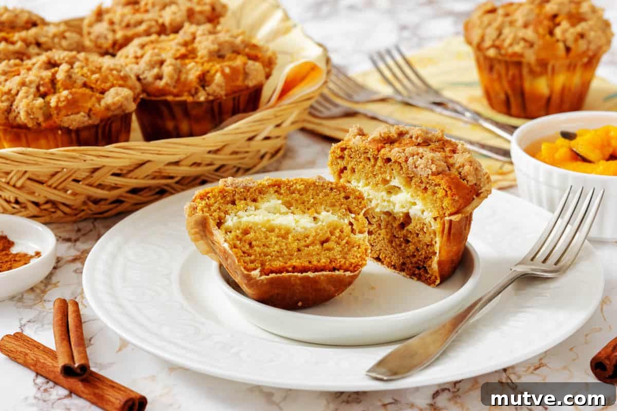 29 Halloween Treats That Beat Your Trick-or-Treat Candy 26 A Pumpkin Cream Cheese Muffins cut in half on a plate reveals a creamy filling, with more muffins in a basket and a bowl of diced fruit in the background.