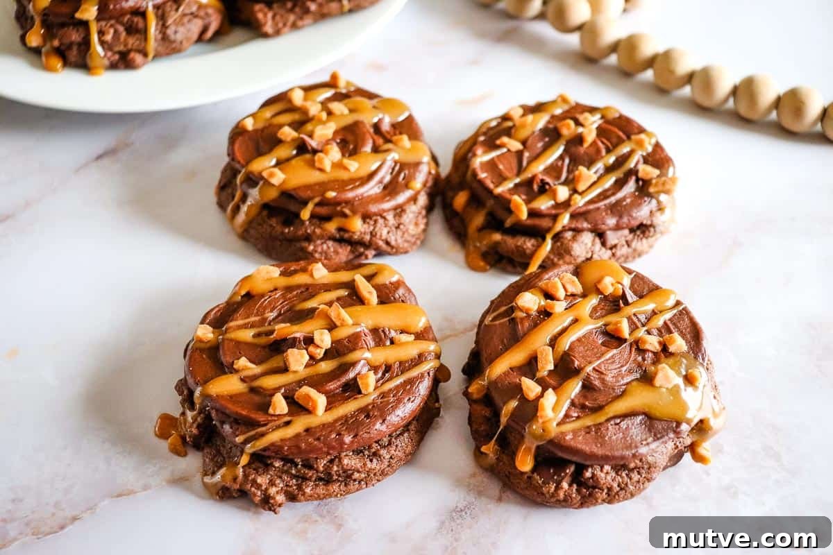 29 Halloween Treats That Beat Your Trick-or-Treat Candy 27 Chocolate Caramel Cookies with frosting, caramel drizzle, and chopped nuts on a white marble surface.