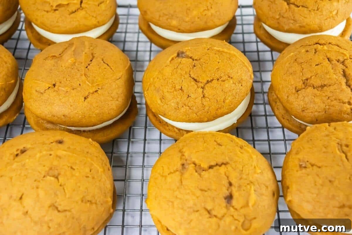 29 Halloween Treats That Beat Your Trick-or-Treat Candy 4 Pumpkin whoopie pies with cream filling are arranged in rows on a wire cooling rack.