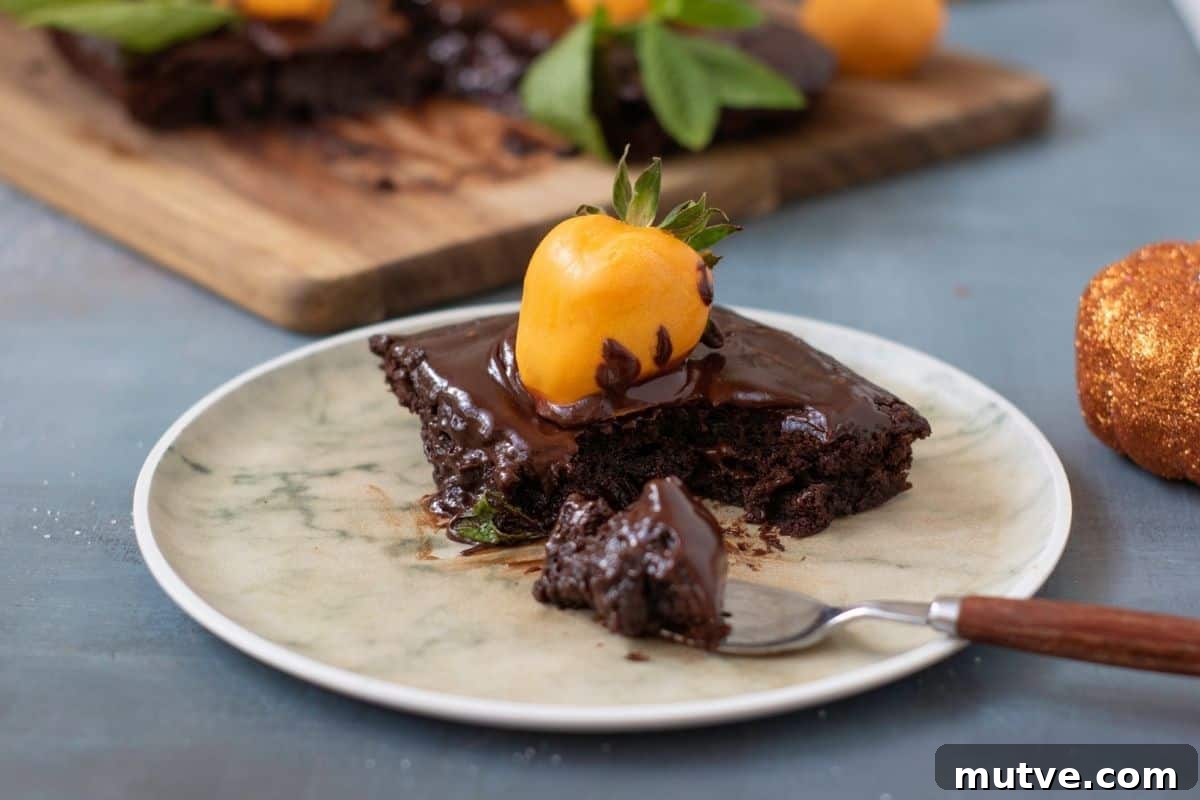 29 Halloween Treats That Beat Your Trick-or-Treat Candy 6 A piece of Pumpkin Patch Brownie Cake. sits on a plate with a fork. More cake is visible in the background on a wooden board.