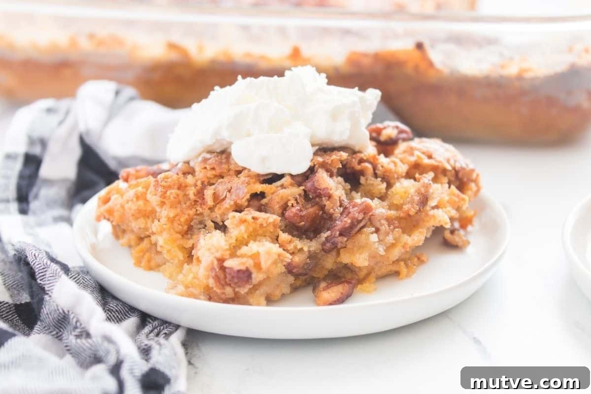 29 Halloween Treats That Beat Your Trick-or-Treat Candy 9 A slice of Pumpkin Crunch Cake on a white plate, topped with whipped cream, with a checkered cloth beside it and a baking dish in the background.