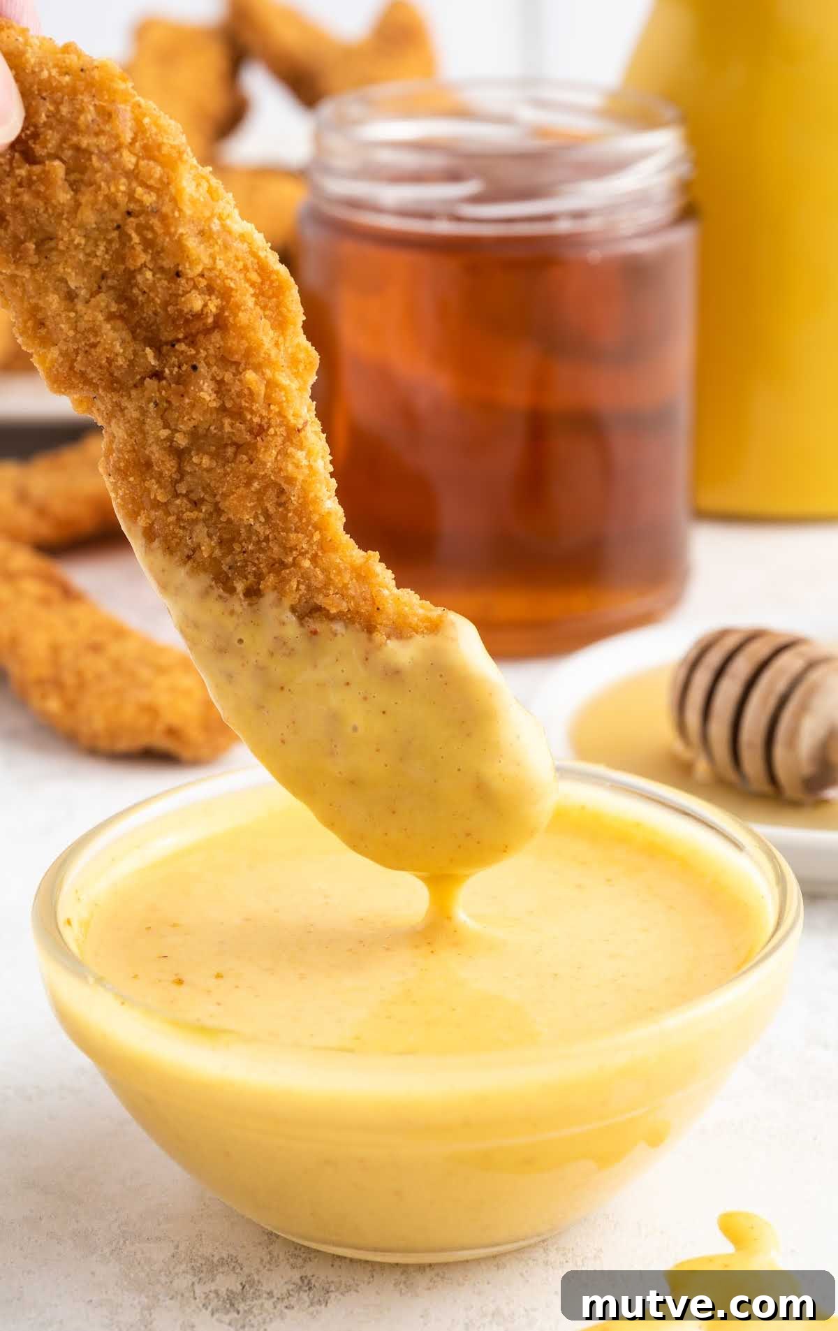 Homemade Honey Mustard Dipping Sauce 6 a close up shot of Honey Mustard Sauce in a bowl with a tender dipped in the sauce