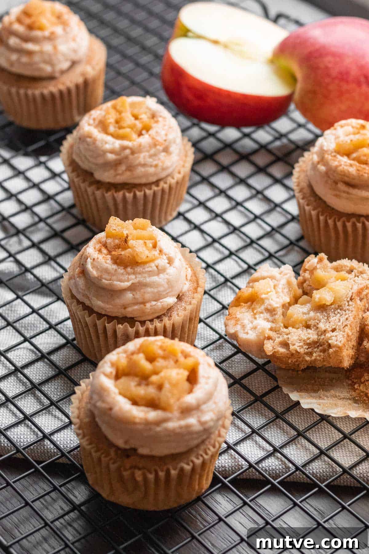 apple pie cupcakes with apple pie filling on top sitting on a wire cooling rack with apple in background