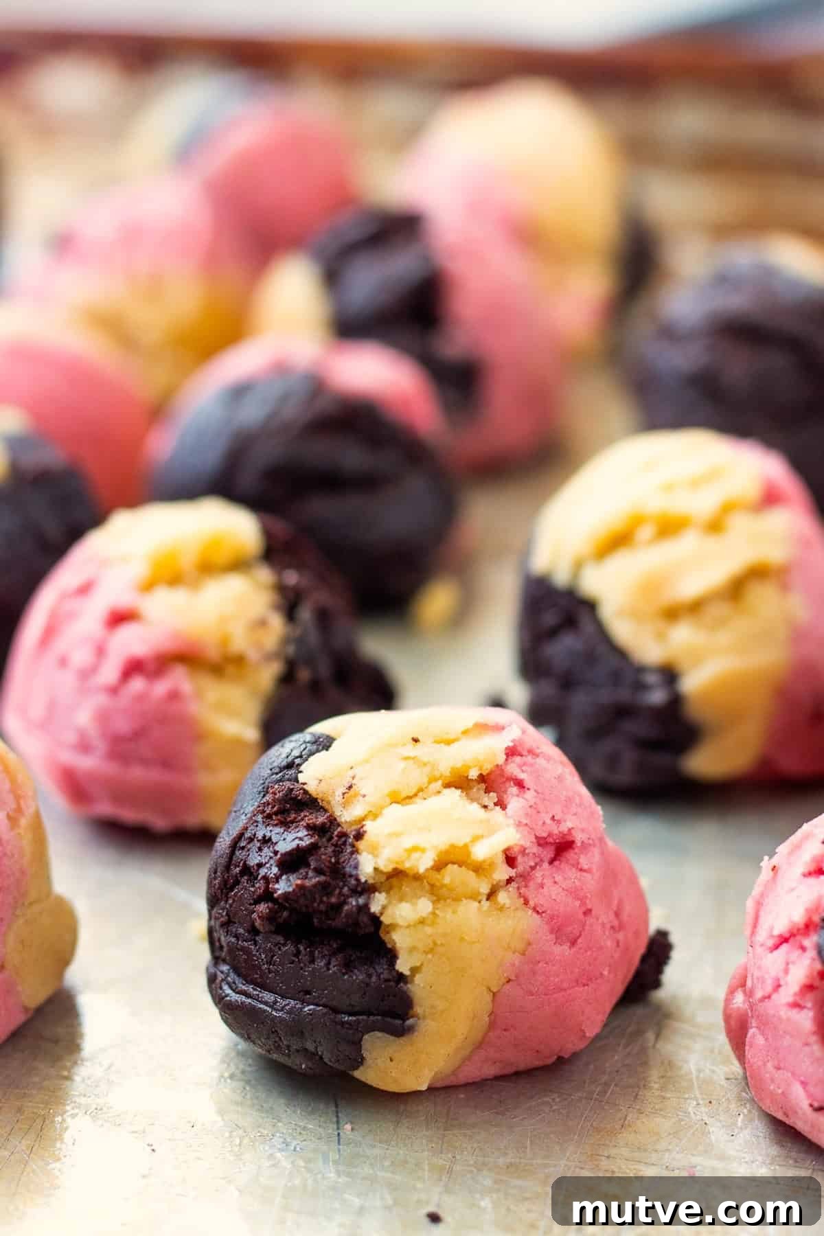 Raw neapolitan cookie dough balls on metal baking sheet.