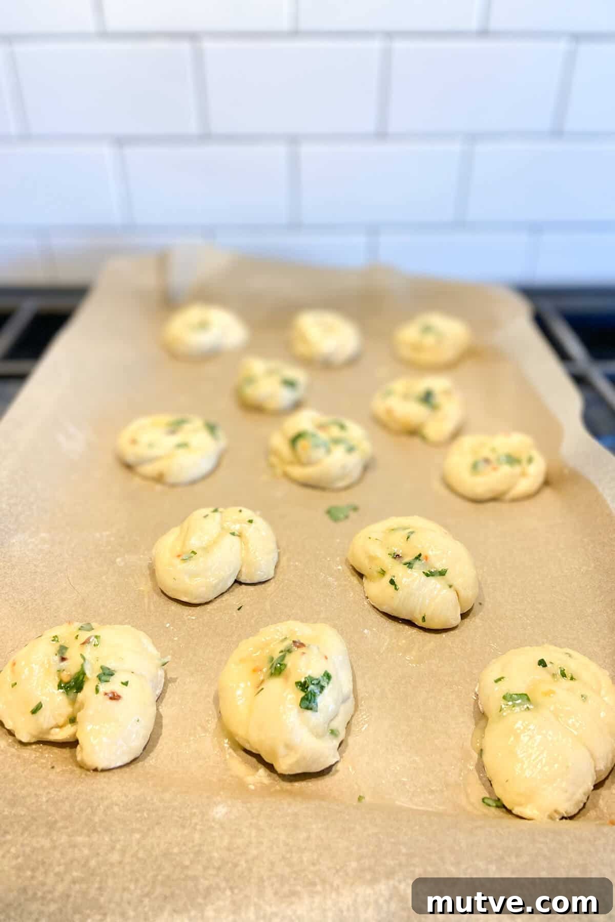 Homemade Garlic Knots Recipe with Herb Butter 13 Knots brushed with garlic butter, on parchment lined baking sheet.