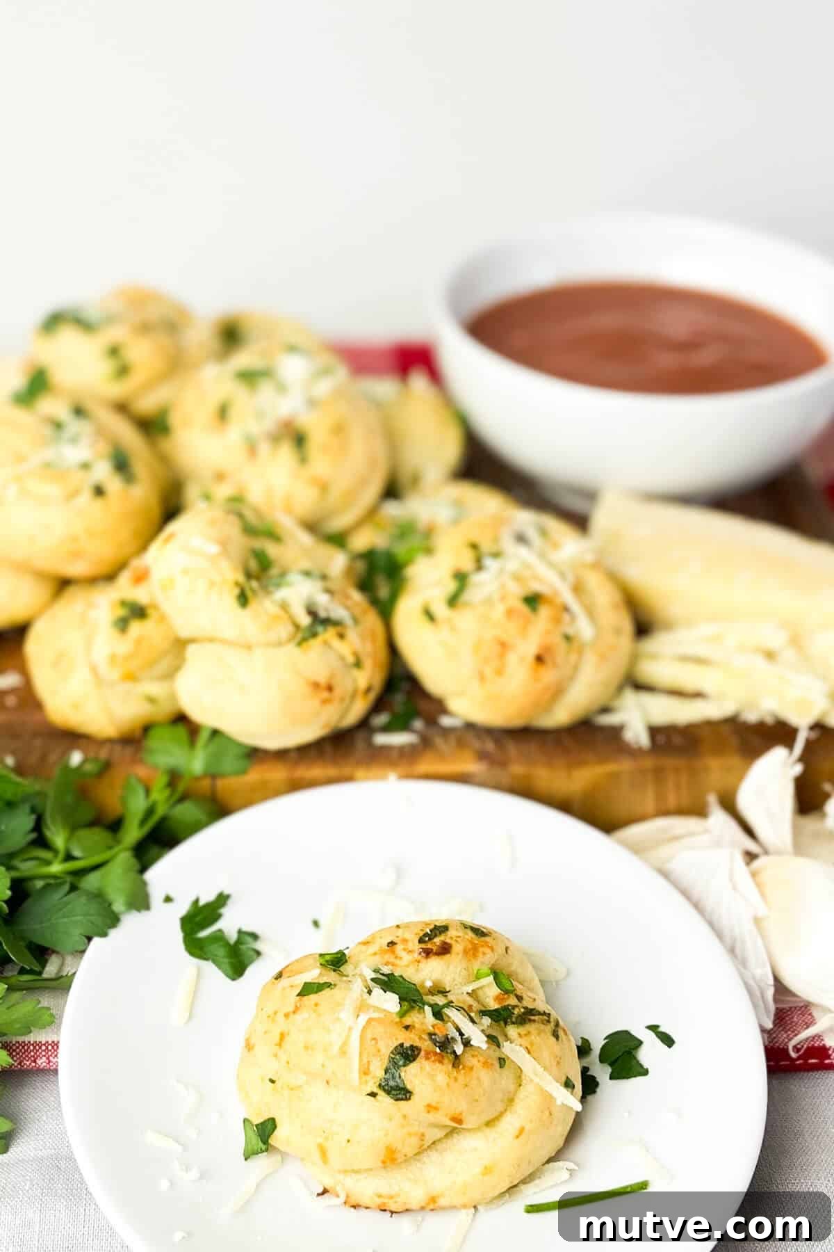 Homemade Garlic Knots Recipe with Herb Butter 14 Serving, with extra cheese, parsley, and marinara sauce.