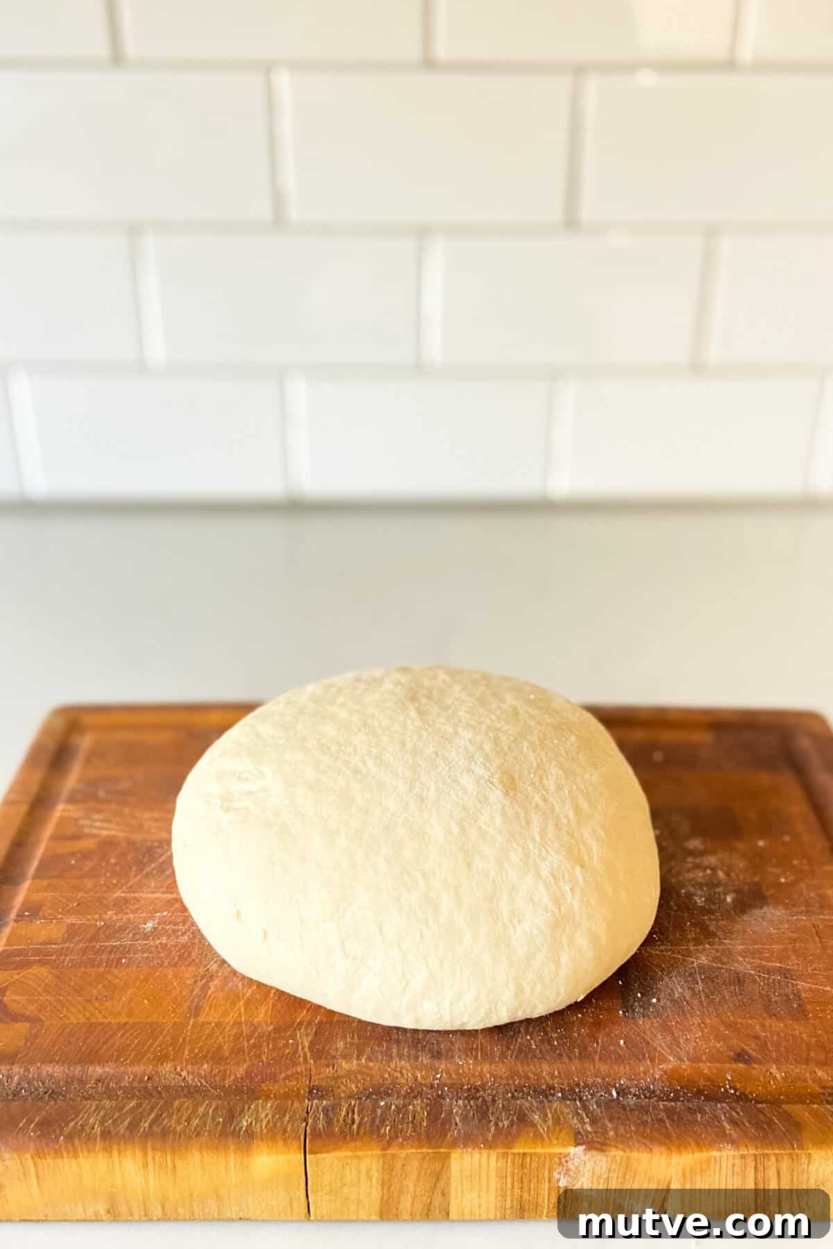 Homemade Garlic Knots Recipe with Herb Butter 9 Dough formed into a ball, on a wooden cutting board.