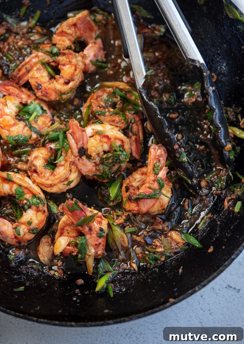 Quick Chili Garlic Shrimp with Chili Crisp Recipe 4 Chili crisp shrimp tossed in cilantro is in the skillet with kitchen tongs.
