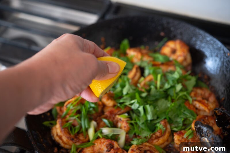 Quick Chili Garlic Shrimp with Chili Crisp Recipe 7 A hand is squeezing out a half lemon to chili shrimp tossed with cilantro.