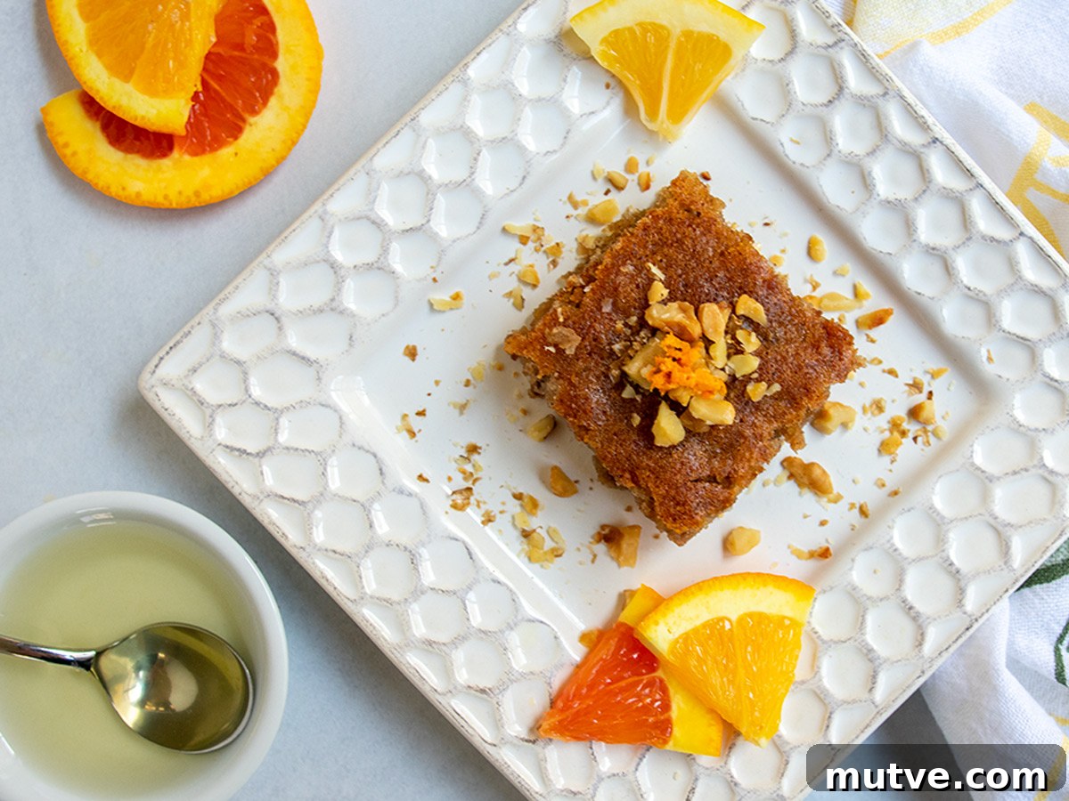 Tishpishti Honey Almond Cake with Citrus Syrup 20 Slice of tishpishti cake on a square plate topped with nuts and orange zest.