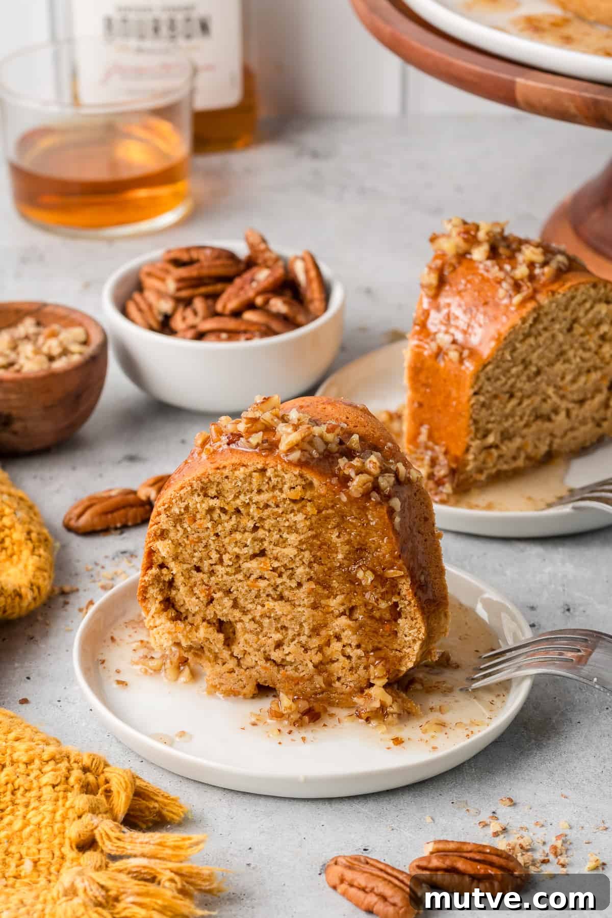 Spiced Sweet Potato Bundt Cake with Maple Glaze 2 Two slices of sweet potato bundt cake on white plates next to a small bowl of pecans.