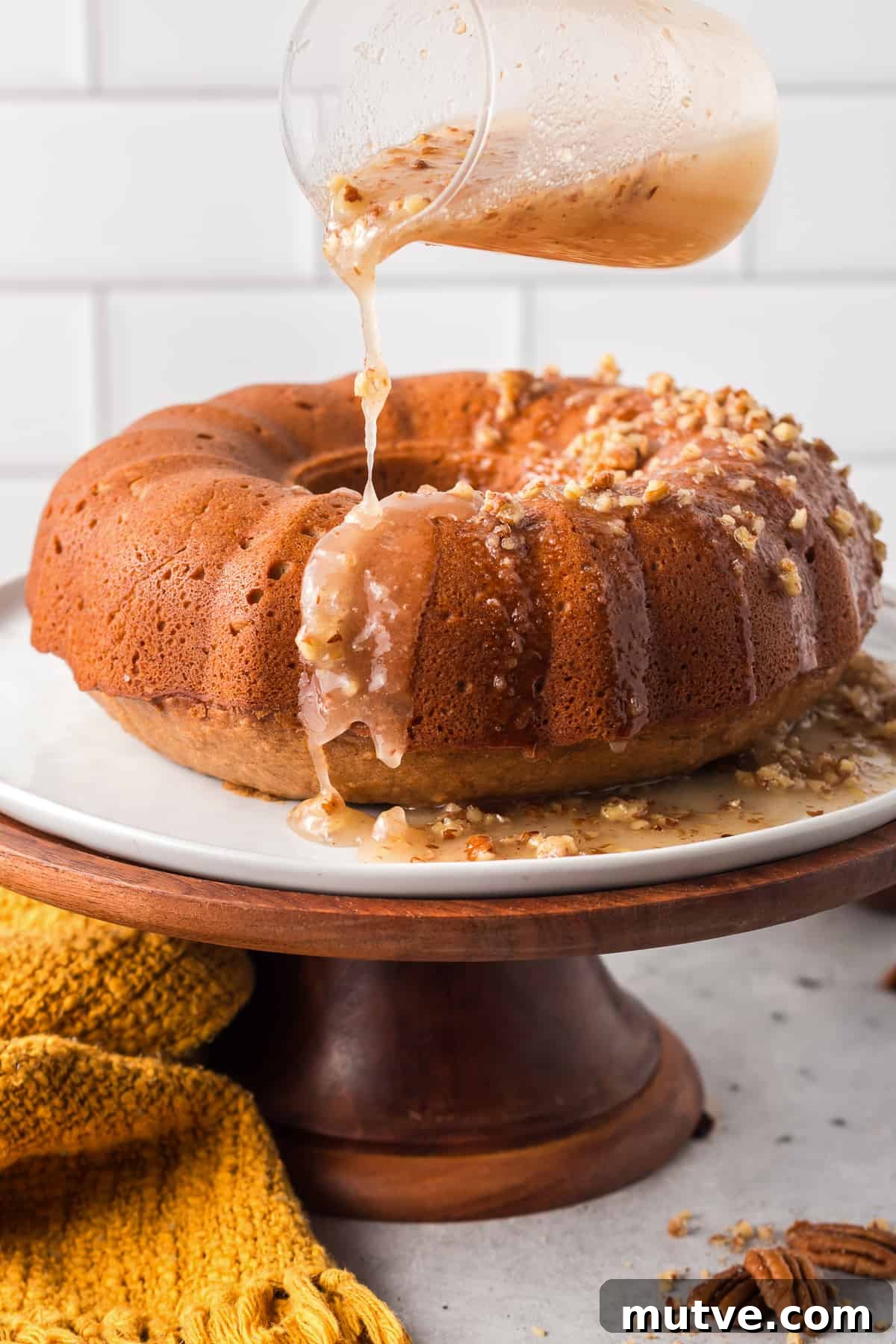 Spiced Sweet Potato Bundt Cake with Maple Glaze 9 Bourbon pecan icing pour over a Bundt cake on a wooden cake pedestal.