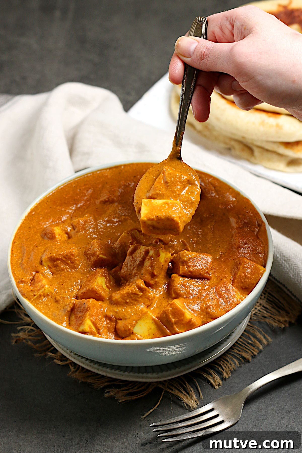 A hand scooping some butter paneer from a bowl with a spoon.