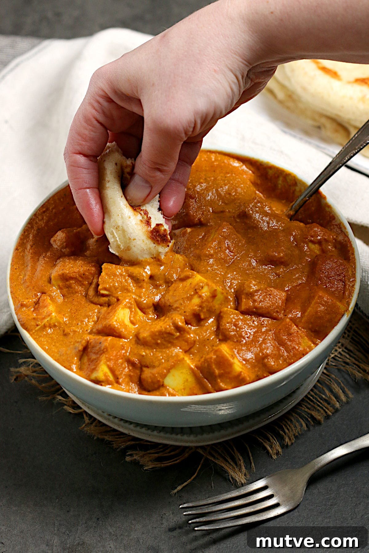 A hand scooping some butter paneer from a bowl with a piece of bread.