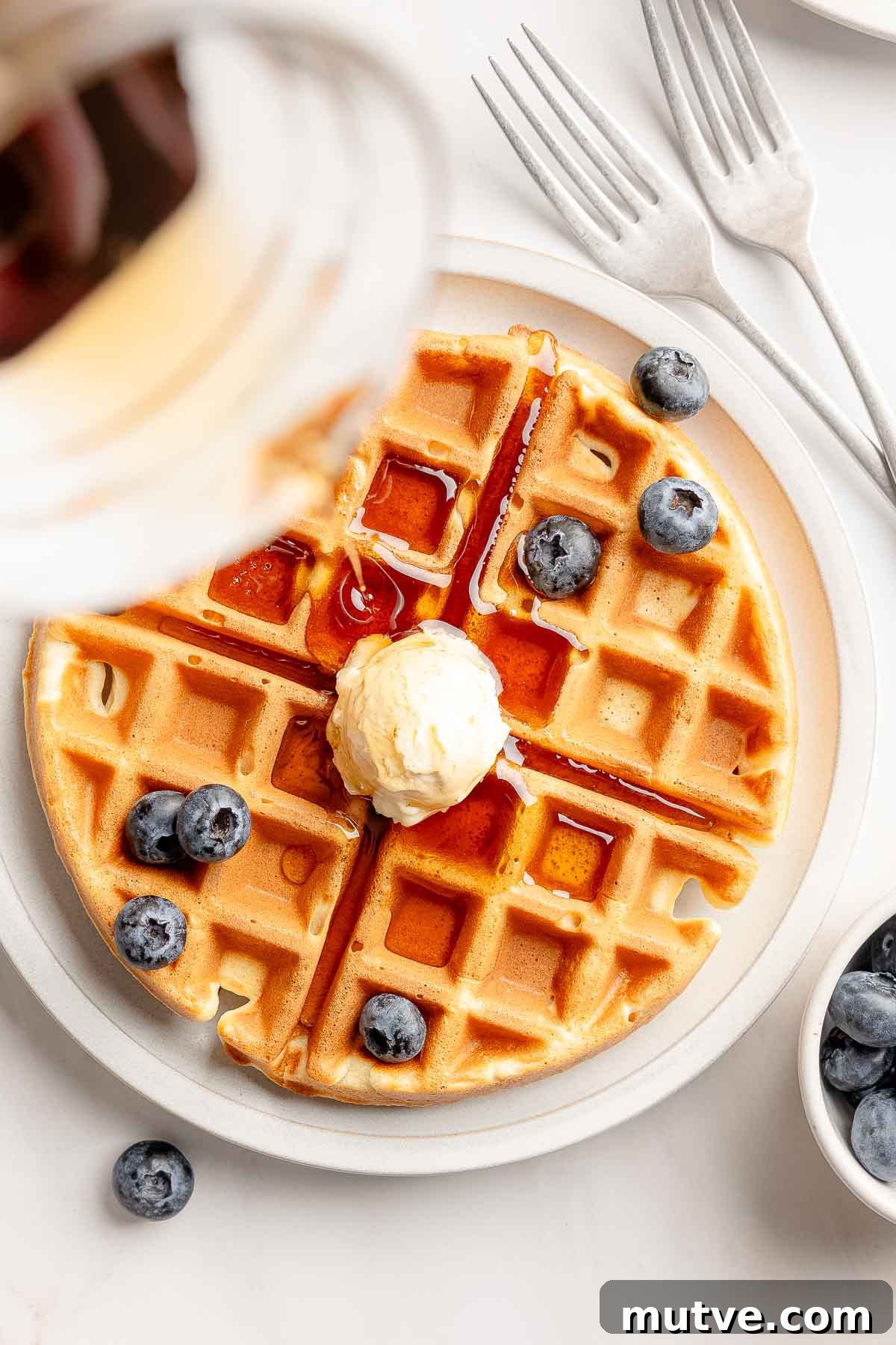 Fluffy Gluten-Free Belgian Waffles Recipe 2 Overhead view of gluten-free waffles garnished with butter and blueberries, is drizzled with syrup.