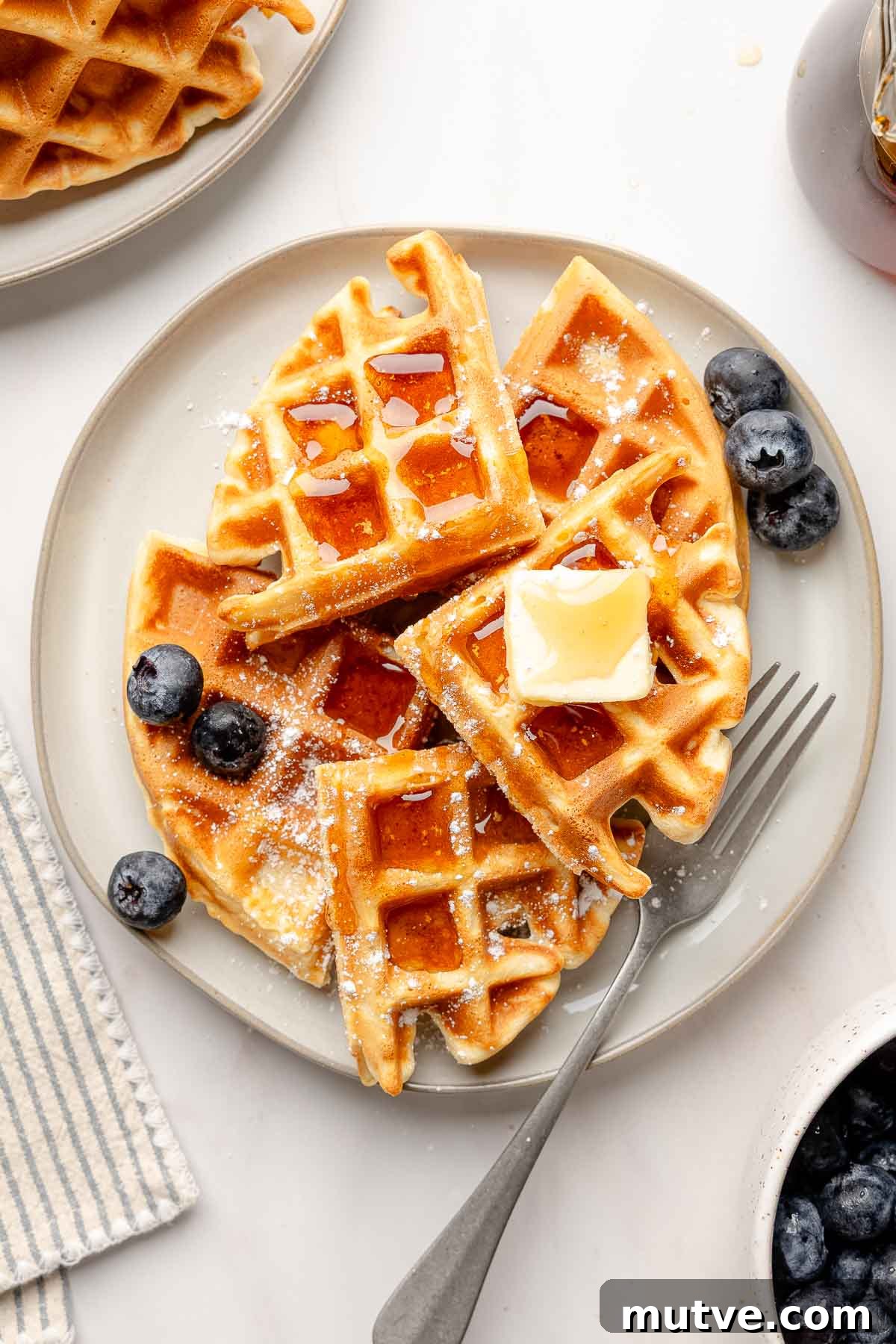 Fluffy Gluten-Free Belgian Waffles Recipe 6 Gluten-free Belgian waffles on a gray plate topped with butter, maple syrup, and powdered sugar, served with fresh blueberries.
