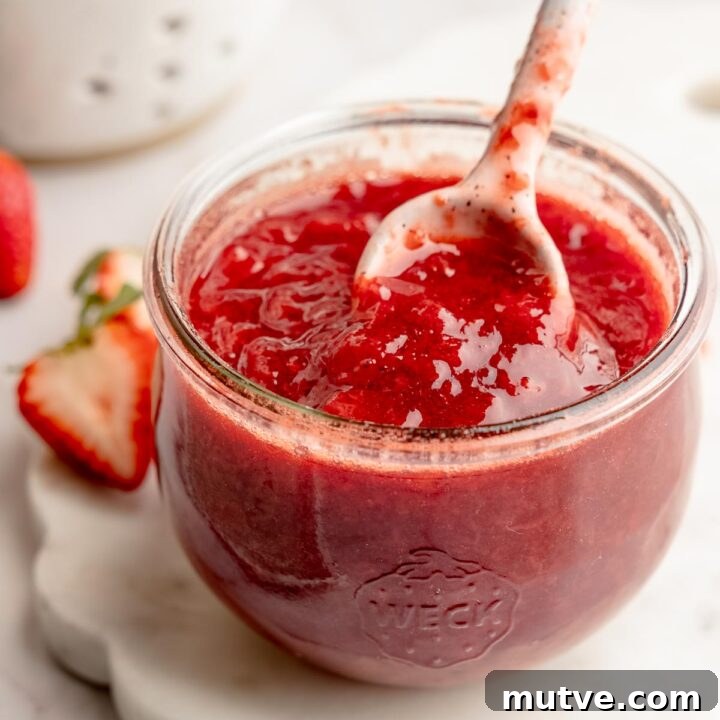 Weck jar filled with strawberry fruit sauce, ceramic spoon lifting sauce.