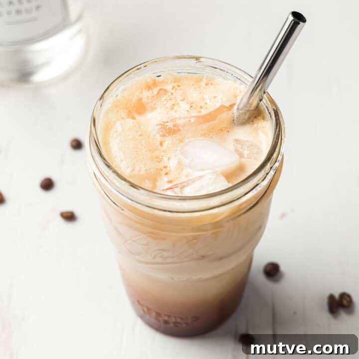 Frothy iced shaken espresso in a mason jar with ice and a stainless steel straw.
