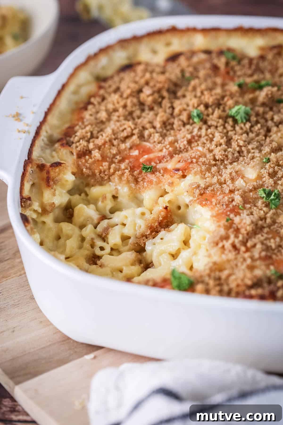 A portion of mac and cheese has been removed from serving dish showing ultra creamy and cheesy sauce clinging to tender macaroni pasta. With a golden crisp topping and fresh parsley.