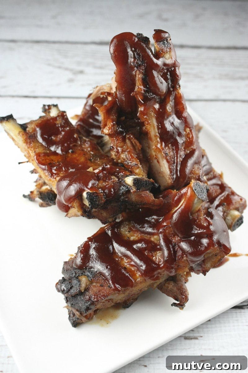 How to Cook the Best Ribs in the Oven ribs on a white plate drizzled with barbecue sauce