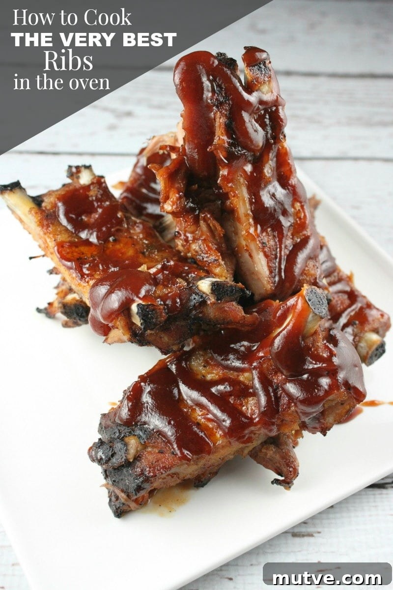 How to Cook the Best Ribs in the Oven ribs on a white plate with barbecue sauce drizzled on top