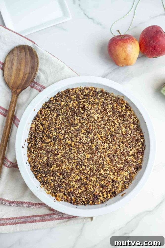 Gluten-Free Apple Crisp Recipe with Oat Crumble 10 overhead photo of gluten free apple crisp in a pie plate on a white and cream stripped towel with a wooden spoon
