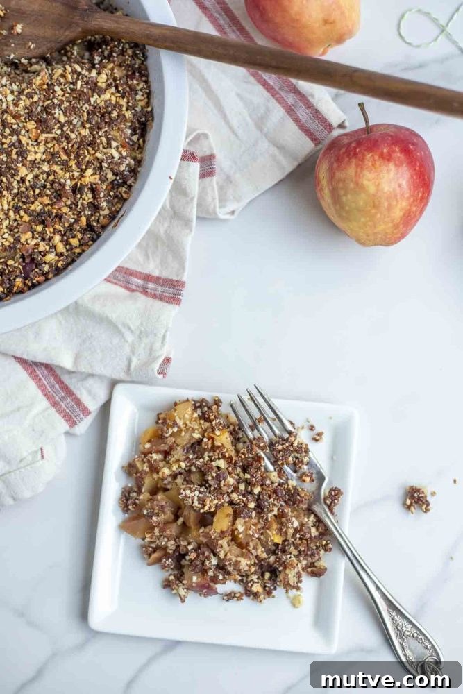 Gluten-Free Apple Crisp Recipe with Oat Crumble 4 overhead photo of apple crisp on a small white plate on a marble countertop with a plat of apple crisp and apples in the background